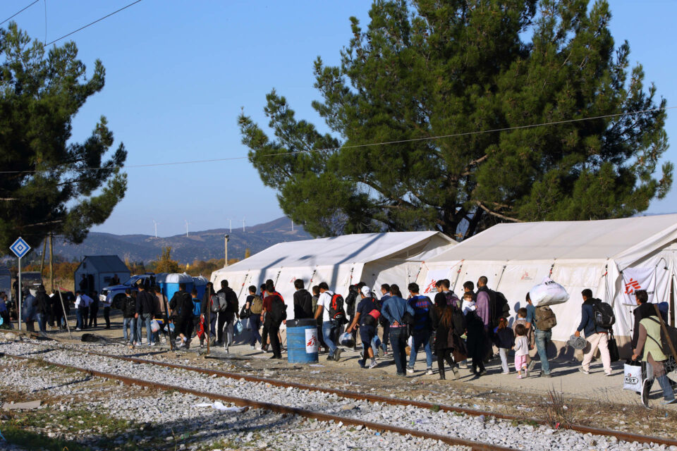 Men and women refugees walking in a line near large tents
