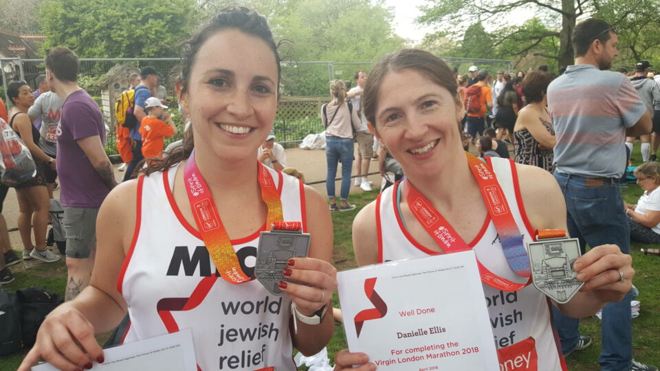Two women smiling holding medals after finishing marathon