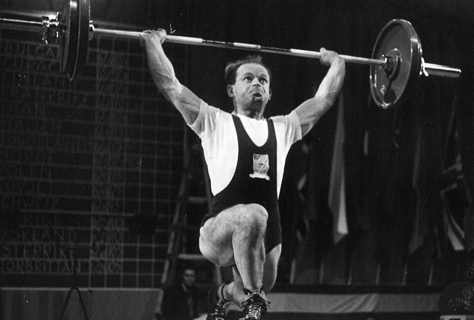 Ben Helfgott lifting a barbell above his head during the olympics