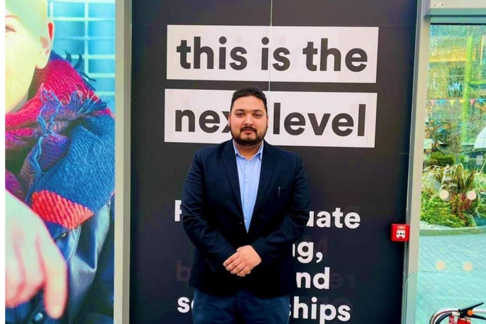 Man facing camera in front of a board saying 'this is the next level'