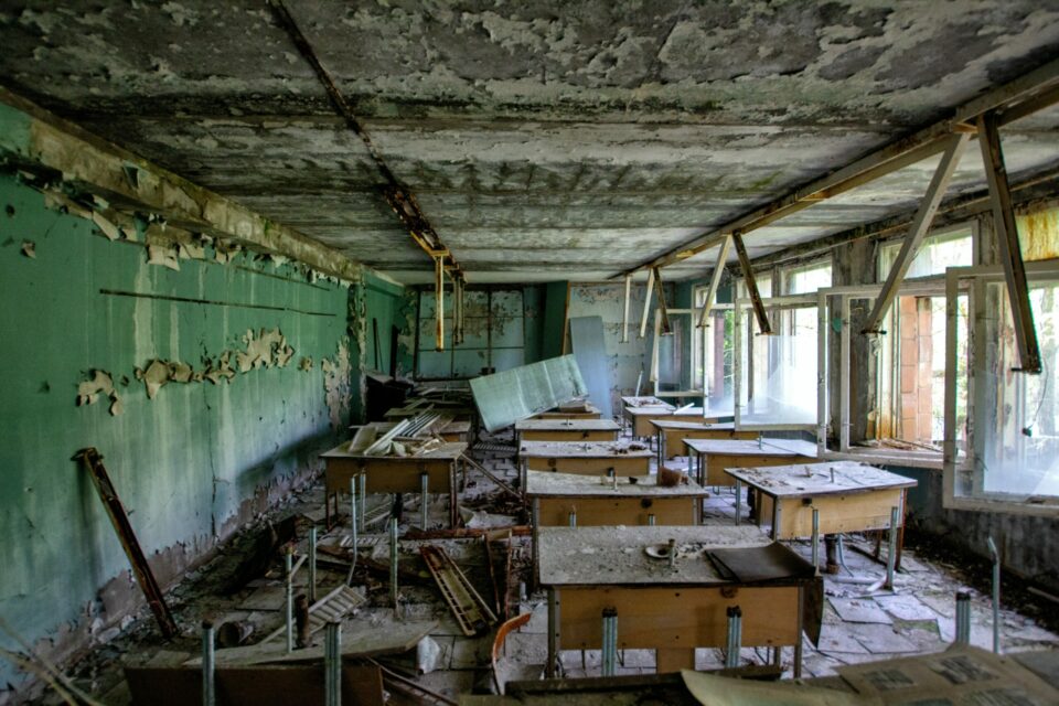 A classroom in disrepair with blown out windows and no one in it
